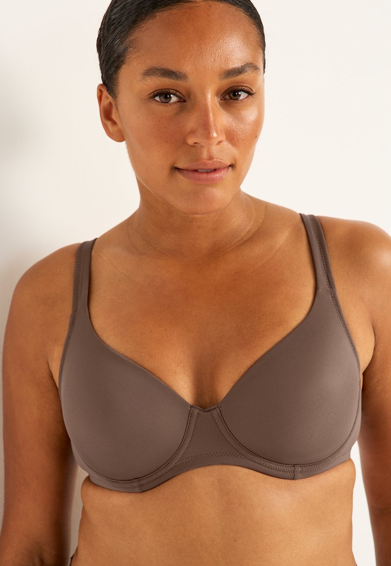 Brun, vadderad behå med justerbara band och slät textur. Har en stödjande design och enkel sömnad längs kanterna.