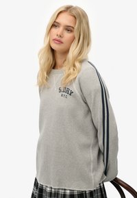 Suéter gris con textura acanalada, rayas marinas en las mangas y logo "S.DRY N.Y.C." en el frente. Dobladillo recto y corte holgado.