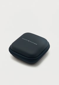 Μικρή μαύρη θήκη με φερμουάρ, με το λογότυπο Tommy Hilfiger και έμβλημα με τη σημαία στην κορυφή, τοποθετημένη σε ένα απλό λευκό φόντο.