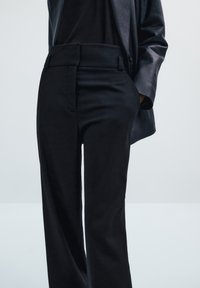 Zwarte op maat gemaakte broek met een gladde textuur, hoge taille, gestructureerde pasvorm en zijzakken, gecombineerd met een strakke zwarte leren jacket.