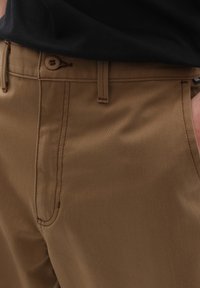 Hnědé kalhoty vyrobené z hladkého materiálu se jednoduchým designem, s uzávěrem na knoflík a švy podél švů.