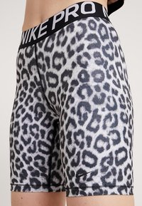 Lyhyet musta-harmaa leopardi kuvioiset shortsit, joissa on musta vyötärö, jossa on "NIKE PRO" -logo. Valmistettu joustavasta kankaasta, jolla on sileä rakenne.