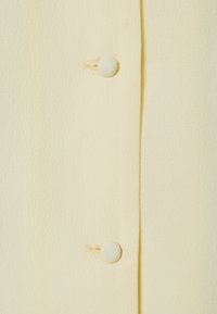 Tissu jaune clair avec une surface texturée, présentant deux boutons recouverts de tissu et un design épuré et simple.