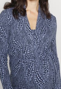 Námořnické modré šaty s puntíkovým vzorem v světle modré. Dlouhé rukávy, zavinovací design a šněrování v pase. Měkká textilie.