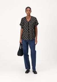 Svart blus med kort ärm och geometriskt mönster, matchad med raka blå denimjeans och en vävd svart handväska.