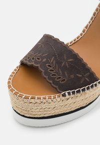 Sandale espadrille en daim marron avec broderie florale, bride à bord festonné, plateforme en jute tissée et semelle en caoutchouc blanche, vue en gros plan.