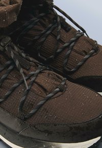 Adidași negri înalți, impermeabili, cu o suprafață texturată, șireturi reflectorizante și talpă de cauciuc, cu picături de apă vizibile.