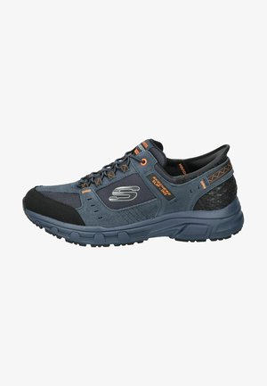 Pánská slip-on obuv Skechers, má tmavě modrý semiš a síťovinový svršek, šedé akcenty, černou gumovou podrážku a strukturovanou zadní část pro podporu.
