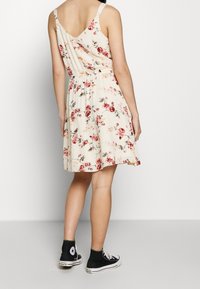 Kwiatowa sukienka na beżowym tle, z luźną spódnicą i regulowanymi ramiączkami, w połączeniu z czarnymi trampkami Converse.