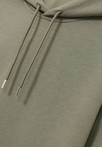 Olijfgroene hoodie met een buidelzak, trekkoordsluiting en zilveren metalen tips op de trekkoorden. Glad textuur van de stof.