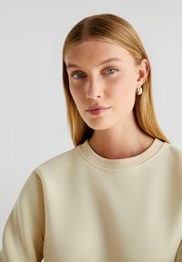 Lichtbeige sweatshirt met een geribde ronde hals. De stof lijkt glad en zacht. Minimalistisch design, geen zichtbare patronen of accenten.