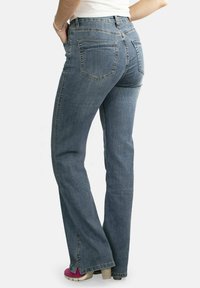 Jeans de mezclilla azul acampanados con un acabado desgastado, dos bolsillos traseros y un ligero deshilachado en el dobladillo, combinados con zapatos de tacón rosados.