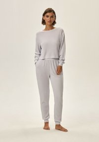 Jasnoszary, prążkowany zestaw odzieży do wypoczynku z długimi rękawami, elastycznym pasem i spodniami zakończonymi mankietami. Miękka faktura, minimalistyczny design, luźny krój.