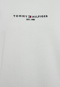 T-shirt en coton blanc avec le texte brodé noir "TOMMY HILFIGER" et "EST. 1985", accompagné d'un design accent rectangulaire rouge et bleu.