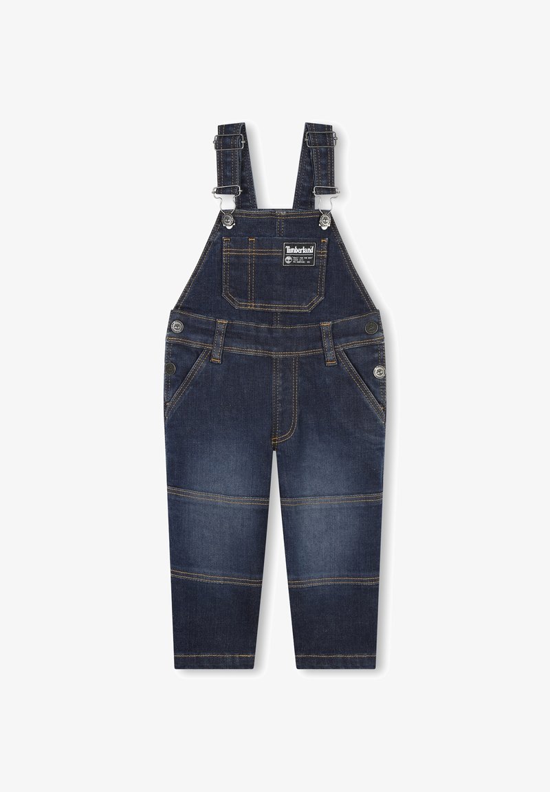 Donkerblauwe denim salopette met verstelbare banden, een voorzak en contrasterende gele stiknaad. Voorzien van knoopsluitingen en taps toelopende pijpen.