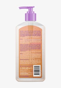 Clear pump bottle of self-tan gel with purple dispenser, orange back label featuring usage instructions, warnings, ingredients, and barcode.