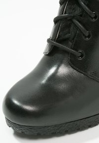 Botte noire en cuir avec texture brillante, bout rond, lacets sur le devant et semelle en caoutchouc robuste pour la stabilité et l'adhérence.