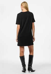 Vestido negro de manga corta con corte relajado, que presenta un escote redondo y una tela texturizada. Combinado con botas de charol negras hasta la rodilla.