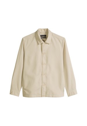 Chemise beige à manches longues avec col, cinq boutons et une petite étiquette sur le côté inférieur, présentée à plat sur un fond blanc.