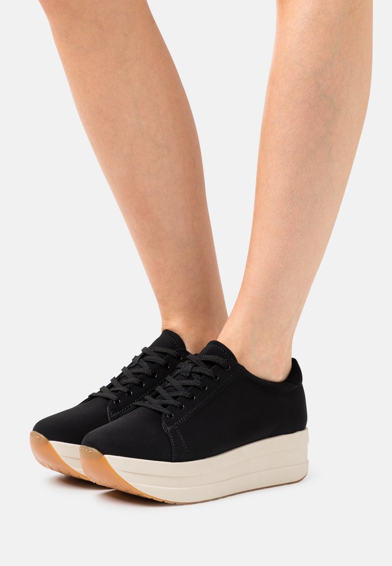 Baskets en tissu noir avec un bout arrondi, une épaisse semelle plateforme crème et des lacets noirs. Semelle extérieure en caoutchouc antidérapante avec un accent gomme.