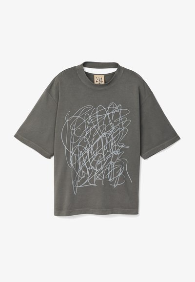 Camiseta de algodón gris con un corte holgado, que presenta un diseño gráfico blanco parecido a un garabato en la parte delantera y un cuello redondo acanalado.