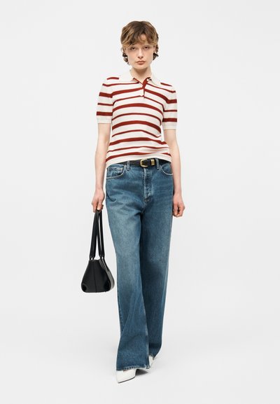 Jeune personne portant un haut à manches courtes rouge et blanc à rayures, un jean bleu à larges jambes, des chaussures blanches, une ceinture noire, et un sac à main noir.