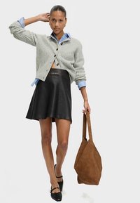 Světlounce šedý pletený kardigan s volným střihem přes světle modrou košili, doplněný černou koženou zvonovou sukní a hnědou kabelkou.