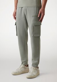 Jasnozielone spodnie cargo z dwoma bocznymi kieszeniami, miękką teksturą materiału, dopasowanym krojem i subtelnym logo "GUESS" z przodu. W połączeniu z białymi sneakersami.