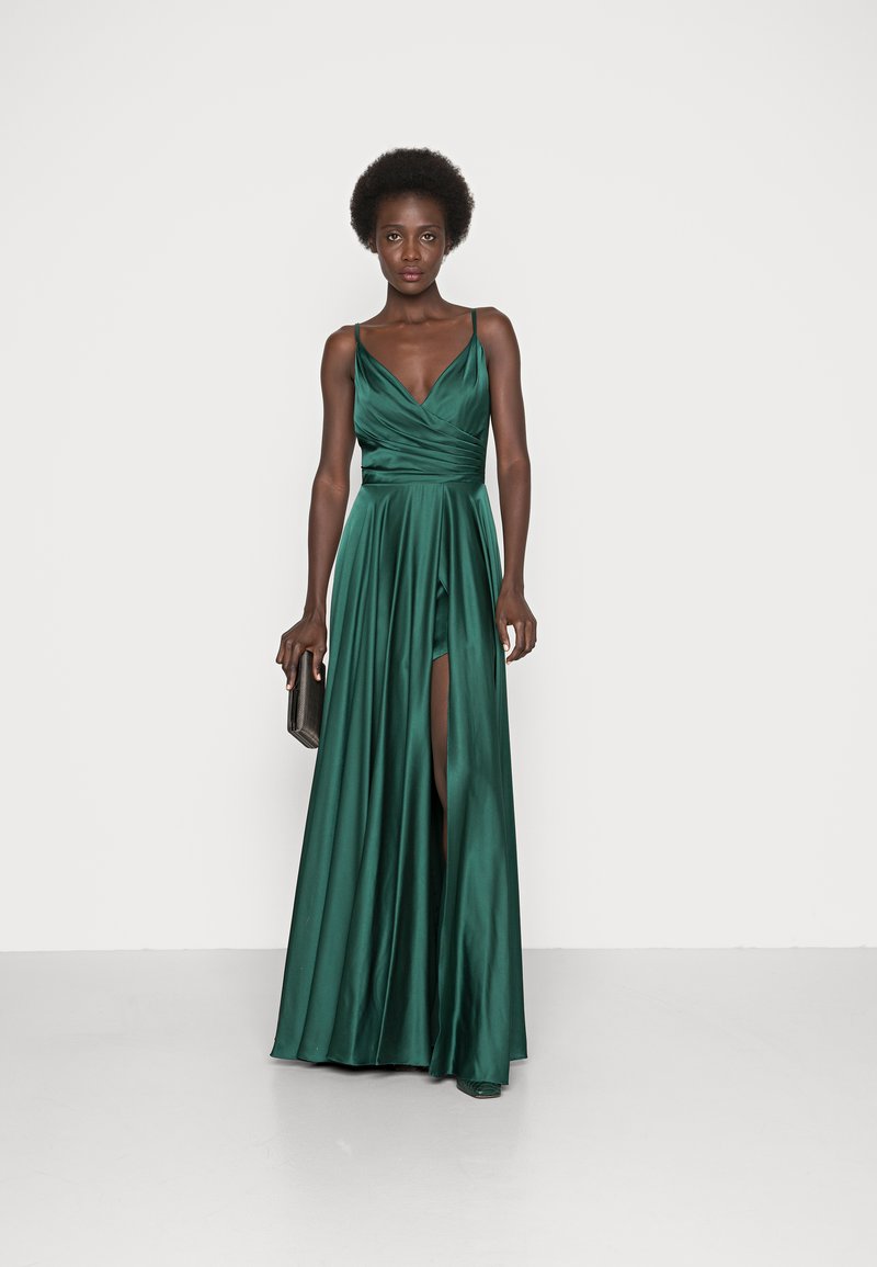 Długa, emeraldowa sukienka z satyny z dekoltem w kształcie litery V, dopasowaną górą i zwiewną spódnicą z wysokim rozcięciem, w połączeniu z czarną kopertówką.