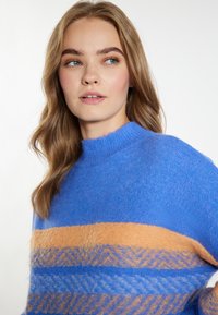 Maglione blu lavorato a maglia con collo alto, caratterizzato da strisce orizzontali arancioni e fantasie, texture morbida e vestibilità ampia.