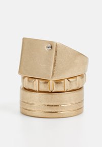 Guldtonet ringsæt med en glat rektangulær top, der har en lille klar ædelsten, lagdelt med teksturerede og polerede bånd nedenfor.