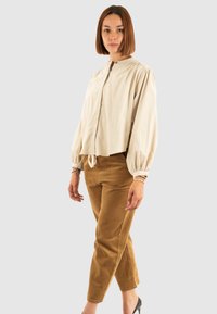 Blusa beige corta con mangas abullonadas y escote redondo. Pantalones de pana marrón con rayas verticales. Modelo lleva tacones negros.