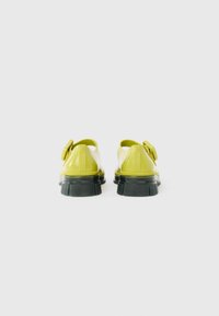Yellow rubber clogs with a back strap, black textured sole, and small decorative bow on the side, showing smooth glossy finish.