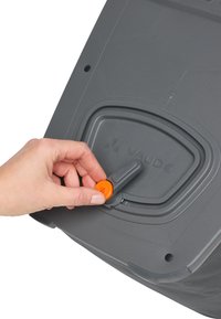 Grijs Vaude-product met een zichtbare oranje verstelknop. Heeft een gestructureerd oppervlak en een duidelijk logo. Hand die de knop bedient.