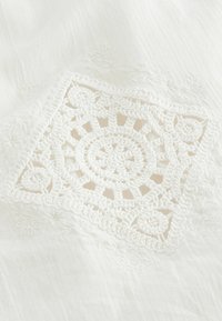Witte stof met ingewikkelde haakdetails in een vierkant ontwerp, met ronde en bloemmotieven in een textuur, zachte afwerking.