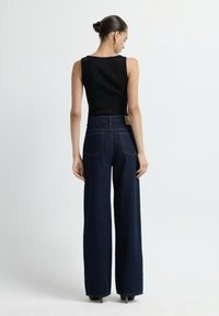 Czarny bezrękawnik oraz ciemnoniebieskie dżinsy o wysokim stanie i szerokich nogawkach z dwiema tylnymi kieszeniami oraz małą jasnobeżową metką na pasku.