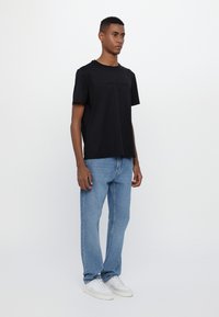 Camiseta gráfica negra de algodón con texto en relieve, combinada con jeans de mezclilla rectos de color azul claro y zapatillas deportivas blancas de perfil bajo.