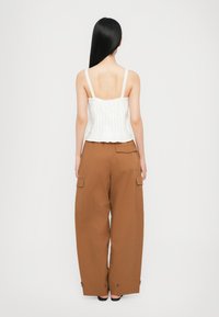 Weißes, plissiertes Crop-Top mit Spitzenverzierungen, kombiniert mit lockeren, braunen Cargo-Hosen mit seitlichen Taschen und einem lässigen Schnitt.