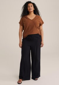 Haut marron à col en v texturé avec des manches retroussées, associé à un pantalon noir ample et des sandales marron. Design simple, coupe décontractée.