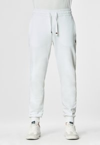 Pantaloni jogger bianchi realizzati in tessuto morbido, con vita regolabile tramite lacci, tasche laterali e polsini a costine. Design minimalista con un branding discreto.