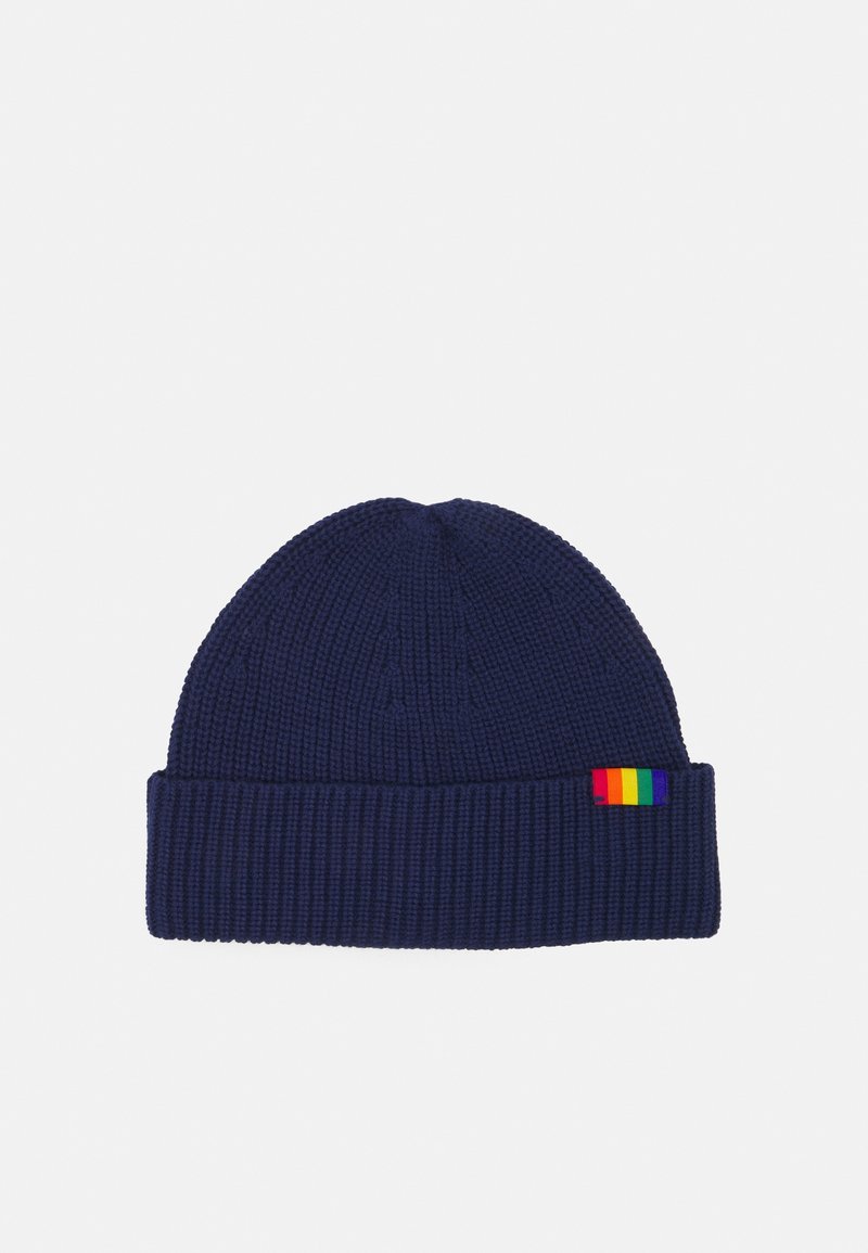 Bonnet tricoté bleu marine avec un revers plié et une petite étiquette rectangulaire rayée arc-en-ciel sur le côté.