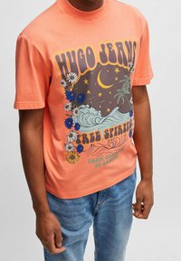 Camiseta de algodón coral de manga corta, con un estampado gráfico que incluye olas, flores y texto en tipografía negrita. Corte casual.