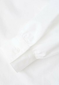 Poignet de chemise blanc avec une texture lisse, une fermeture à bouton unique et des coutures nettes le long du bord. Design simple et minimaliste.