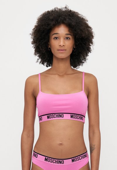 Rózsaszín pamut bralette vékony pántokkal és fekete Moschino logós pánttal. A dizájn négyzet alakú dekoltázst és sima textúrát mutat.
