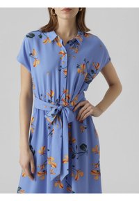 Vaaleansininen mekko lyhyillä hihoilla, kukkakuosi oranssilla ja vihreällä, napitus, kireä vyötärö kankaasta valmistetulla solmittavalla vyöllä, lentävä tekstuuri.