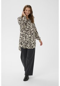 Chemise à manches longues avec un motif de feuilles noir et crème, associée à un jean noir à jambes larges et des bottes noires à la cheville. Texture lisse, coupe décontractée.