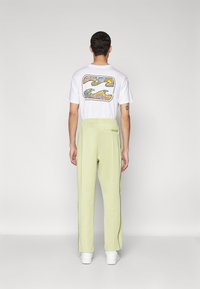 White T-shirt with colorful graphic on back, paired with light green sweatpants and white sneakers, featuring elastic waistband and zipper pocket.
