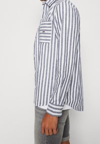 Koszula na guziki w niebiesko-białe paski z kieszenią na piersi. Wykonana z tkaniny o teksturze, posiada kołnierzyk i mankiety.