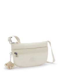 Beige stof skuldertaske med en glat tekstur, frontlomme med lynlås og et rundt logo. Indeholder en aftagelig nøglering med en blød abe.