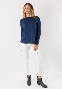 Maglietta navy a maniche lunghe con vestibilità comoda, abbinata a pantaloni bianchi slim-fit e stivaletti neri alla caviglia. Tessuto liscio con una leggera lucentezza.